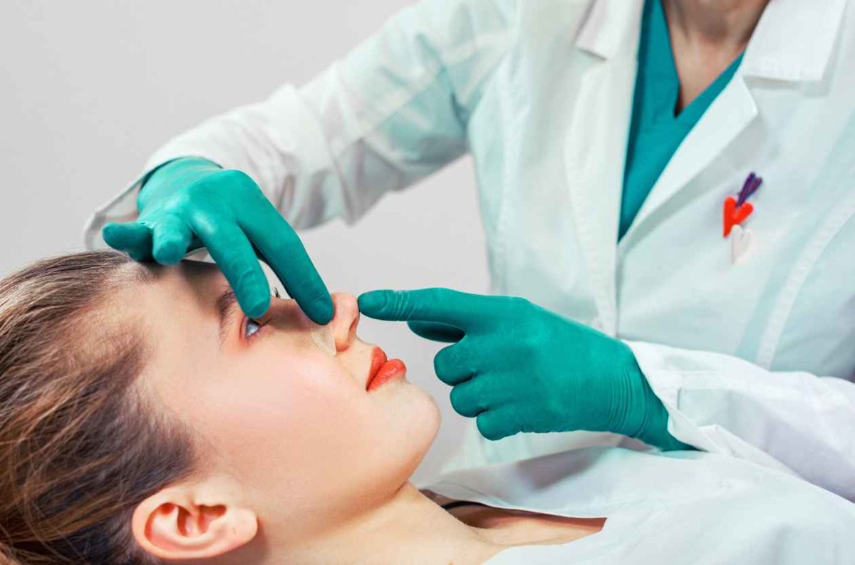 Rhinoplasty, the surgeon hands touches the patient's nose. People, cosmetology, plastic surgery and beauty concept - surgeon or cosmetologist hands touching female face