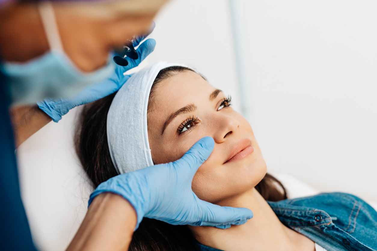 Attractive young woman is getting a rejuvenating facial injections at beauty clinic. The expert beautician is filling female wrinkles using fillers.